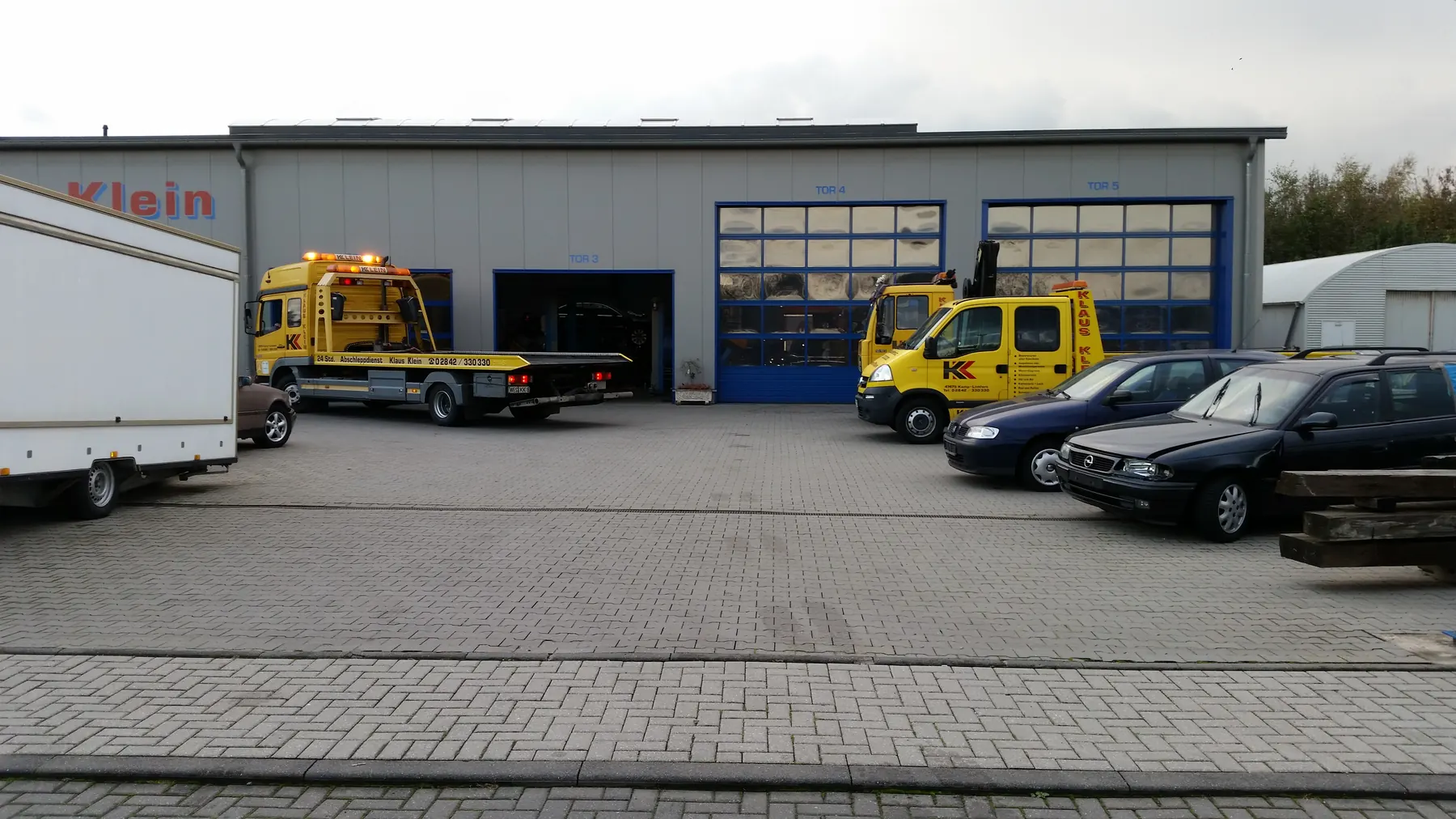 Hof vor der Halle mit zwei gelben Abschleppwagen und Kundenfahrzeugen